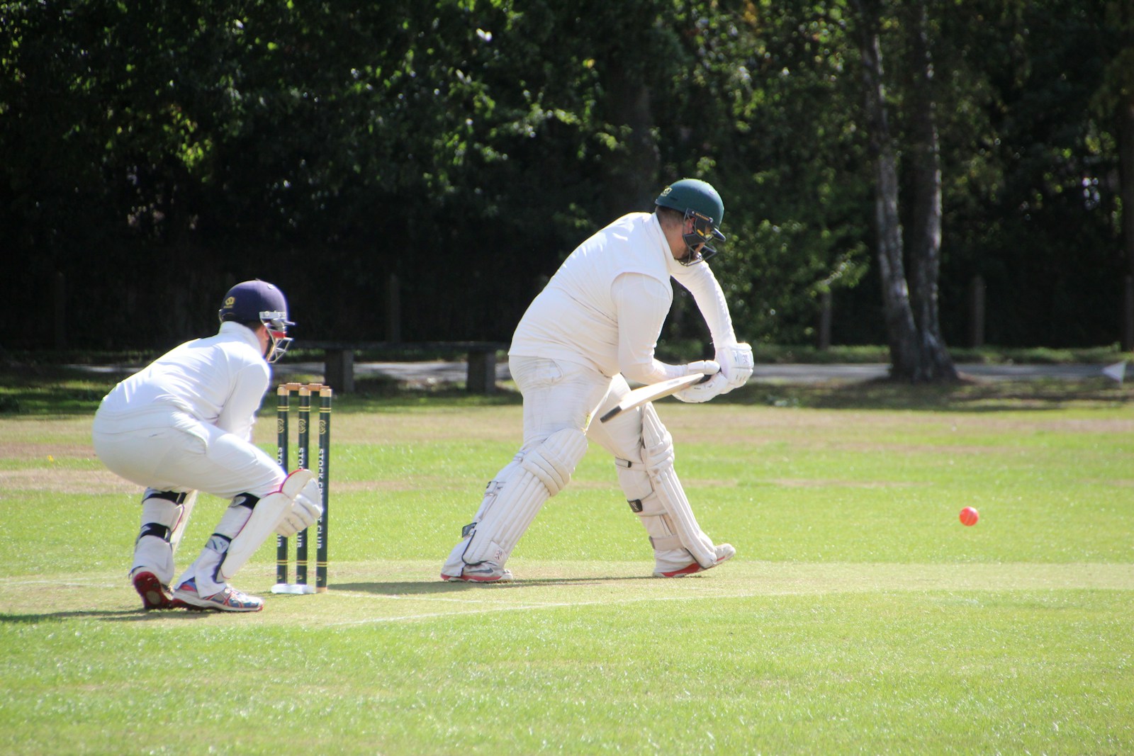 A club cricketer in whites playing a shot, with the wicketkeeper behind the stumps
